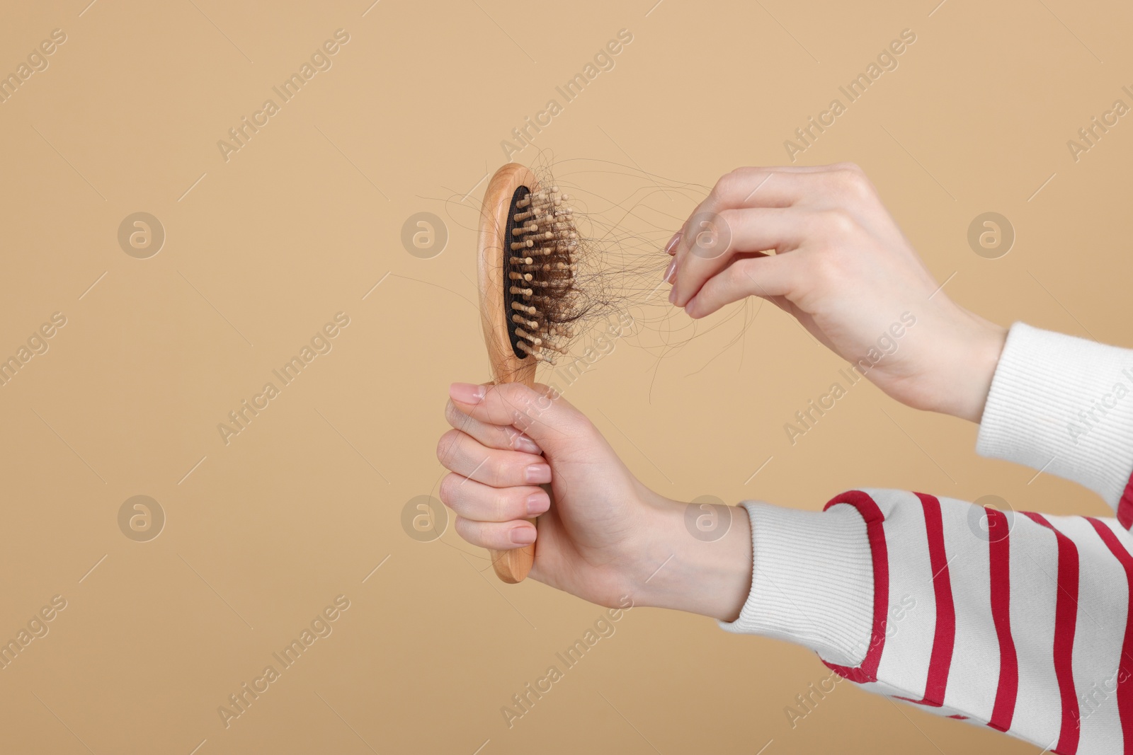 Photo of Woman holding brush with lost hair on beige background, closeup and space for text. Alopecia problem