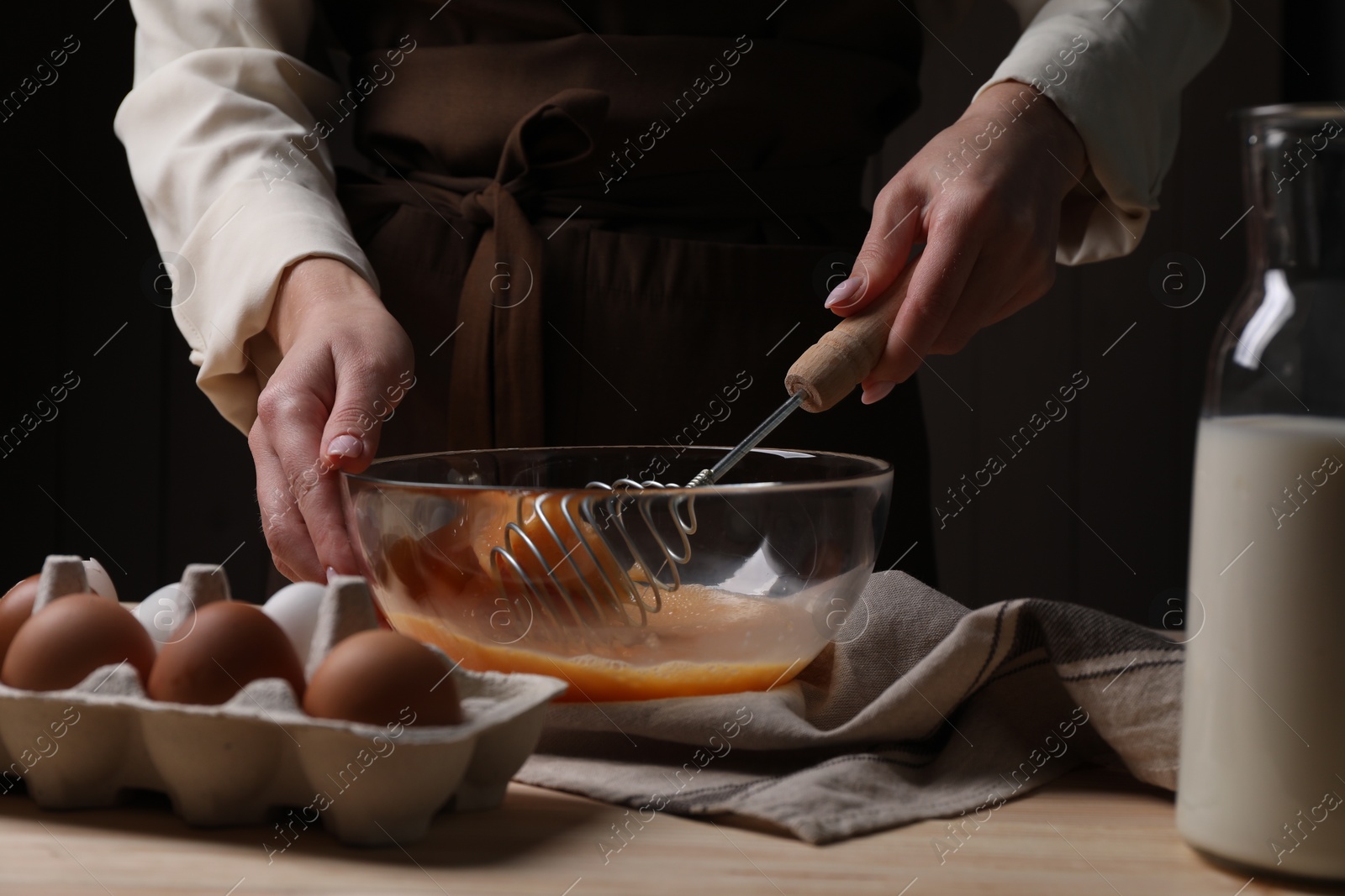 Photo of Woman whisking eggs in bowl at table, closeup