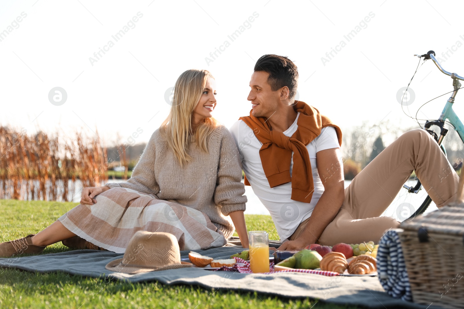 Photo of Happy young couple having picnic near lake on sunny day