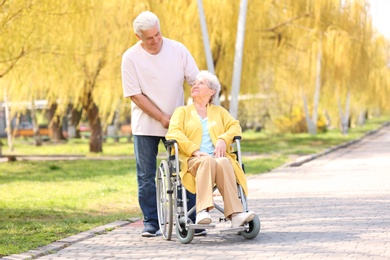 Photo of Senior woman in wheelchair and mature man on sunny day outdoors