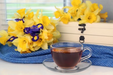 Cup of aromatic tea, beautiful yellow daffodil and iris flowers on windowsill