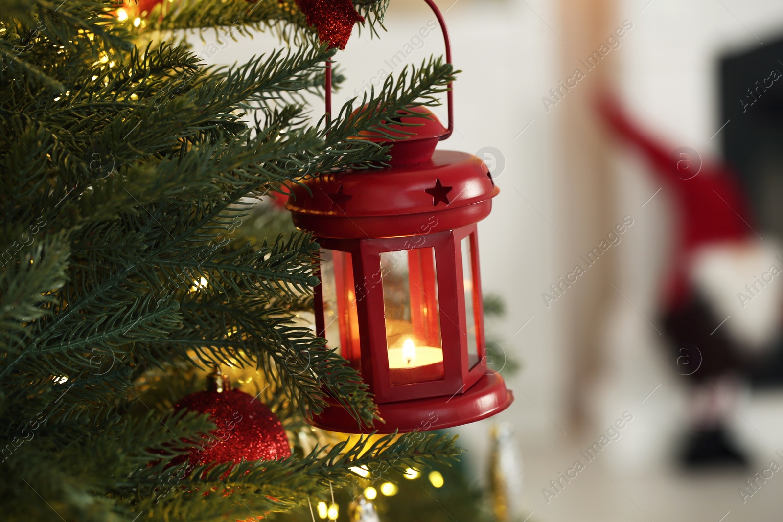 Photo of Christmas lantern with burning candle on fir tree indoors, closeup