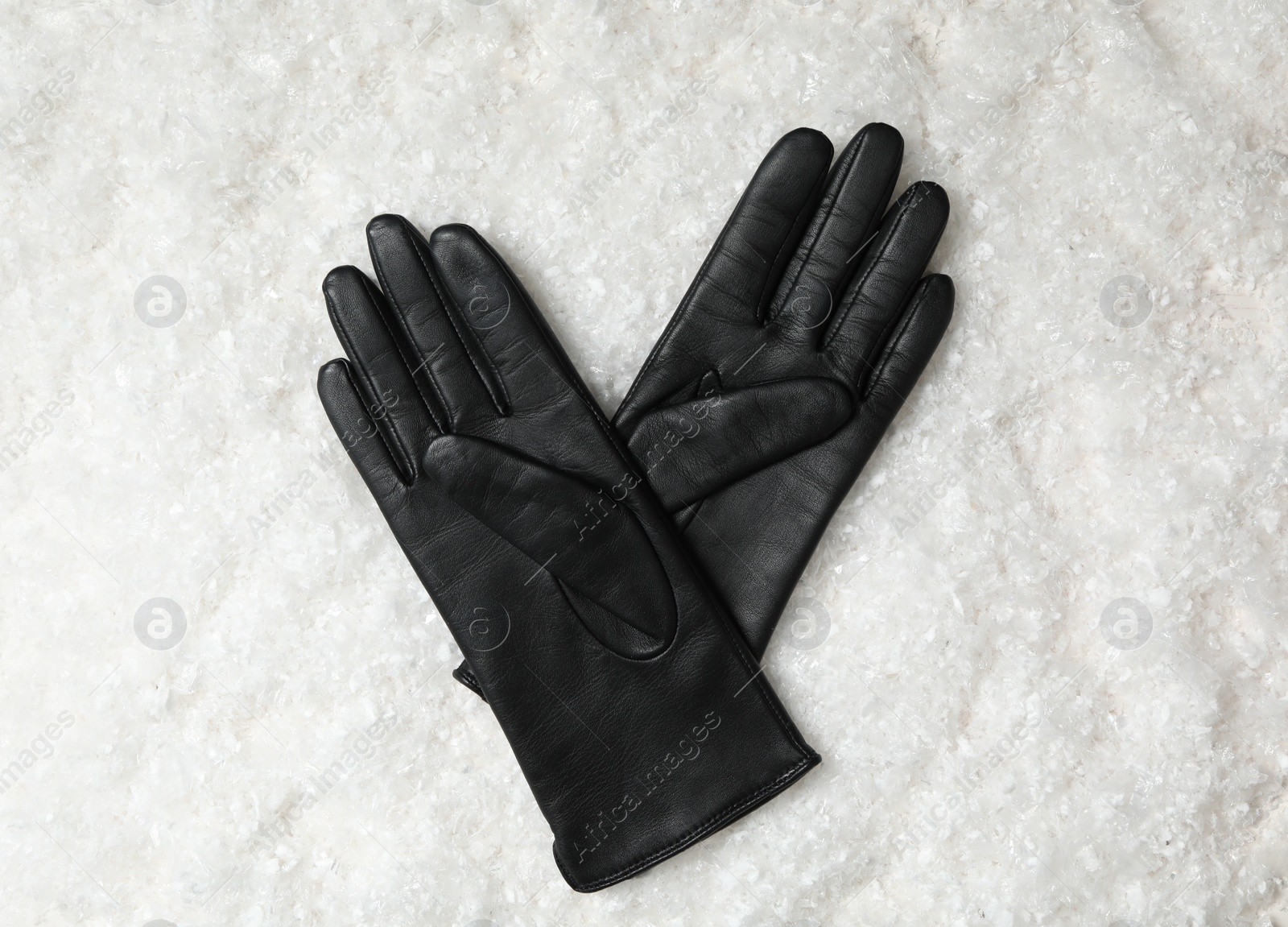 Photo of Stylish black leather gloves on artificial snow, top view