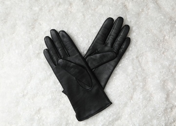 Photo of Stylish black leather gloves on artificial snow, top view