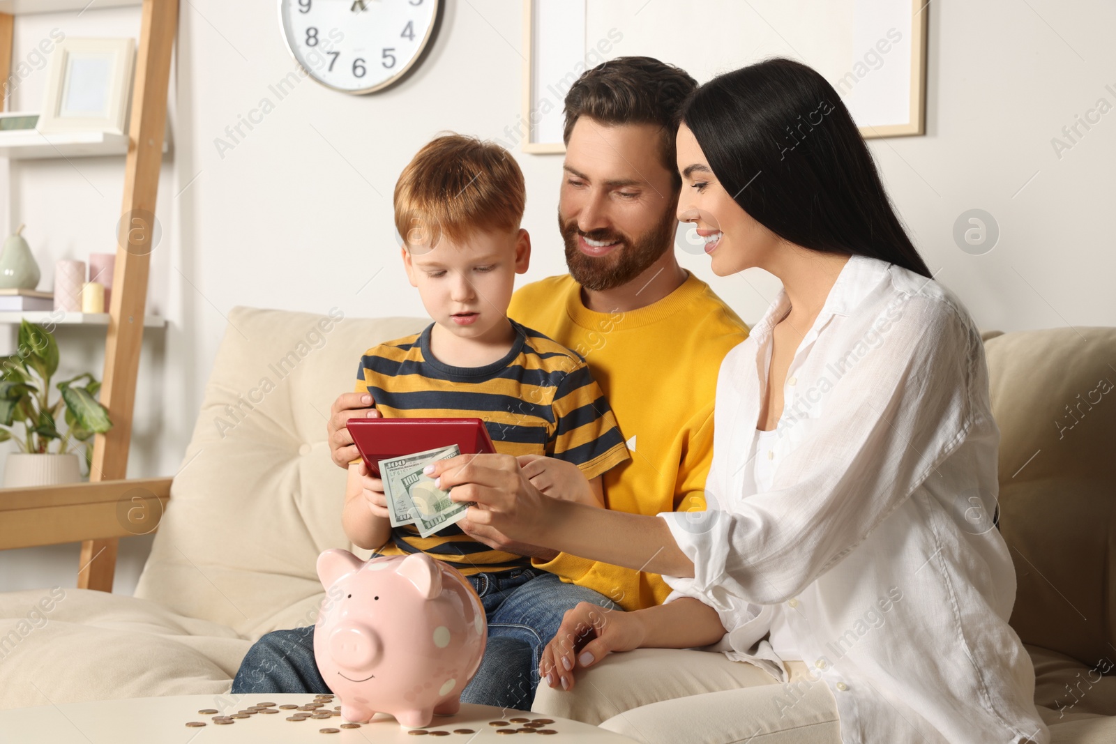 Photo of Happy family with calculator putting money into piggy bank at home