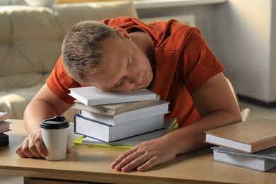 Tired man sleeping near books at wooden table indoors