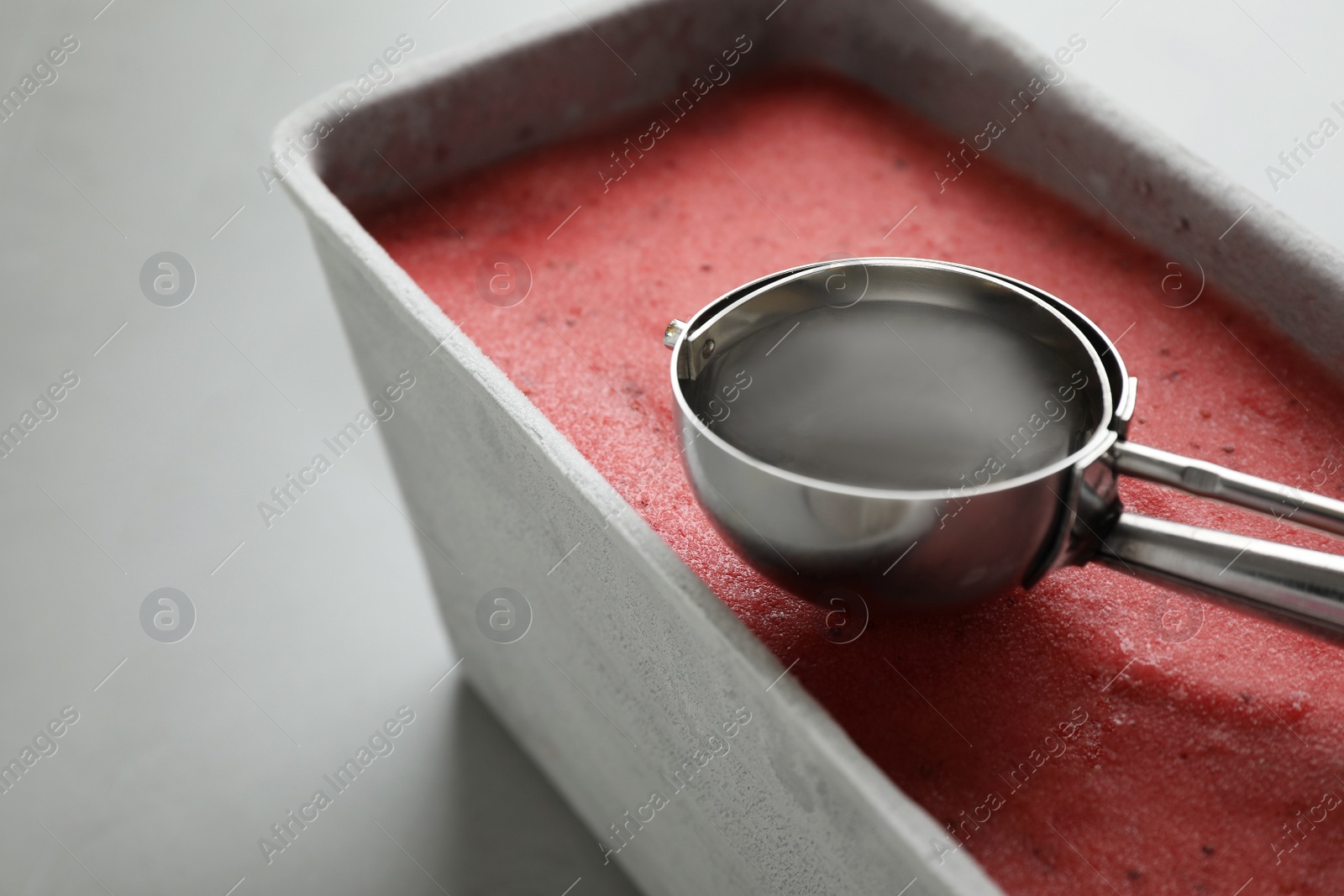 Photo of Container with delicious pink ice cream and scoop on grey table, closeup