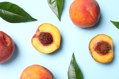 Photo of Delicious juicy peaches and leaves on light blue background, flat lay
