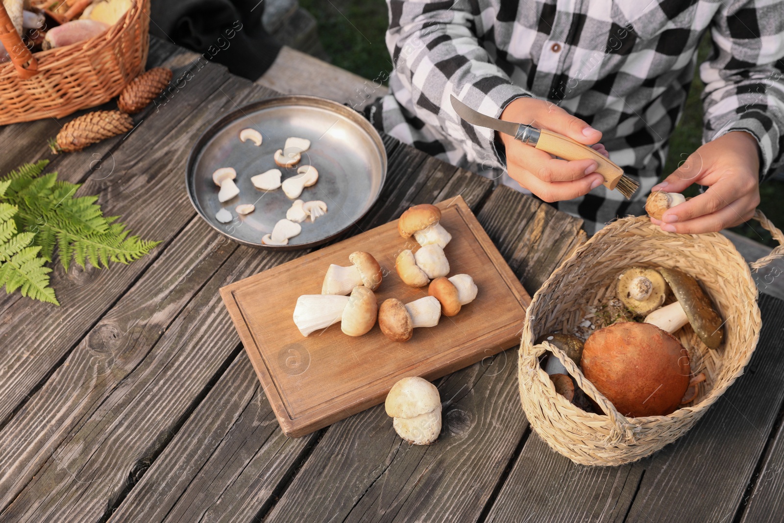 Photo of Man peeling fresh mushrooms with knife at wooden table outdoors, closeup