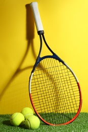 Tennis racket and balls on green grass against yellow background. Sports equipment