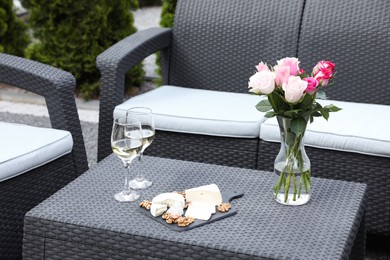 Vase with roses, glasses of wine and food on rattan table on outdoor terrace