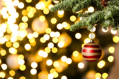 Beautiful Christmas ball hanging on fir tree branch against blurred lights, closeup. Space for text