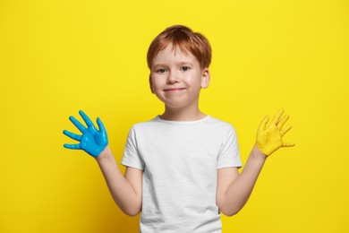 Photo of Little boy with hands painted in Ukrainian flag colors on yellow background. Love Ukraine concept