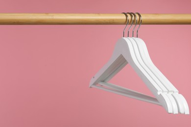 Photo of White clothes hangers on wooden rack against pink background. Space for text