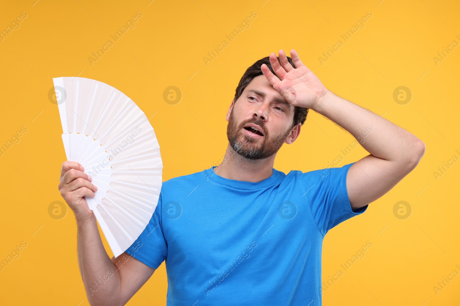 Photo of Unhappy man with hand fan suffering from heat on orange background