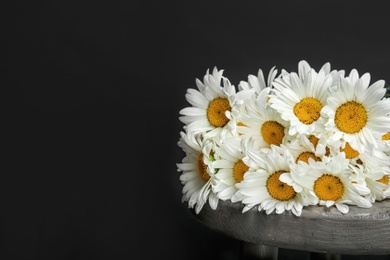 Beautiful chamomile flowers on table against dark background