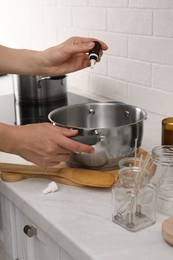 Photo of Woman adding essential oil into pot with melted wax at kitchen counter, closeup. Making homemade candles