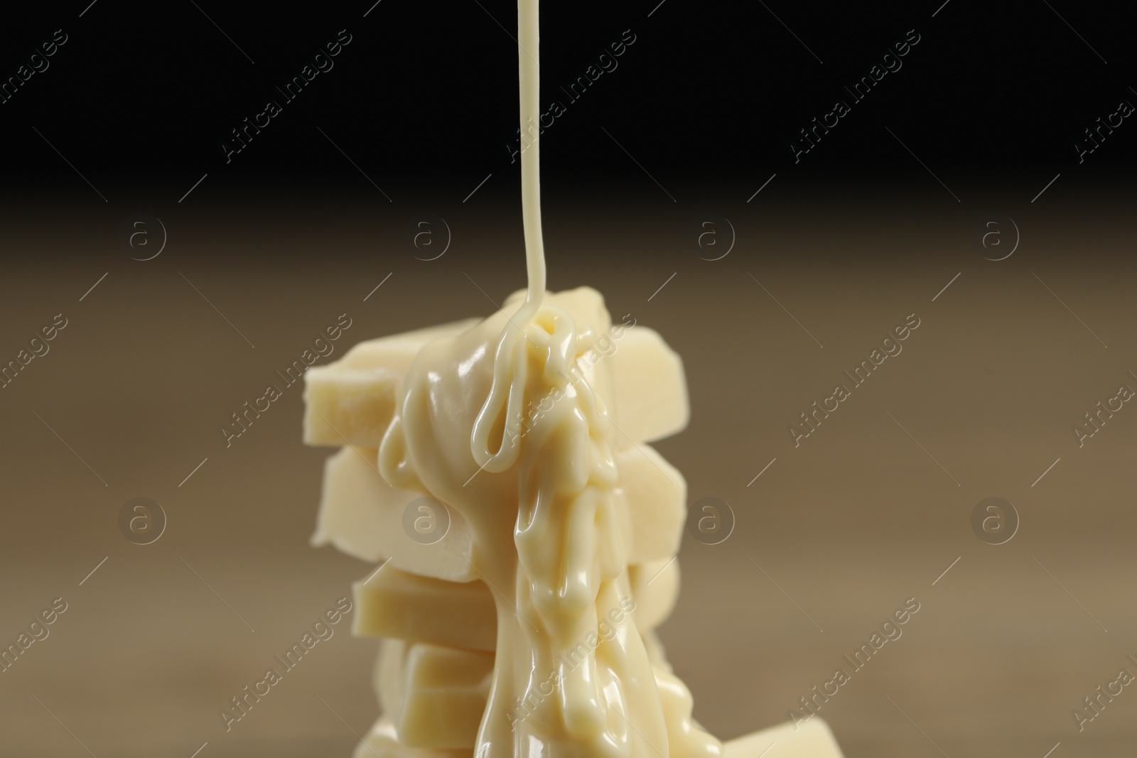 Photo of Pouring tasty white chocolate paste onto pieces against blurred background, closeup