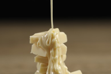 Pouring tasty white chocolate paste onto pieces against blurred background, closeup