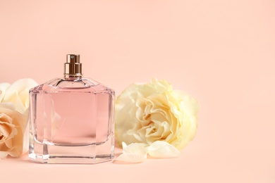 Photo of Bottle of perfume and beautiful flowers on beige background. Space for text