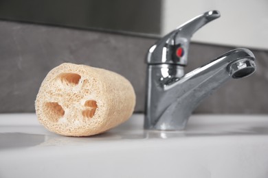 Natural loofah sponge on washbasin near faucet, closeup