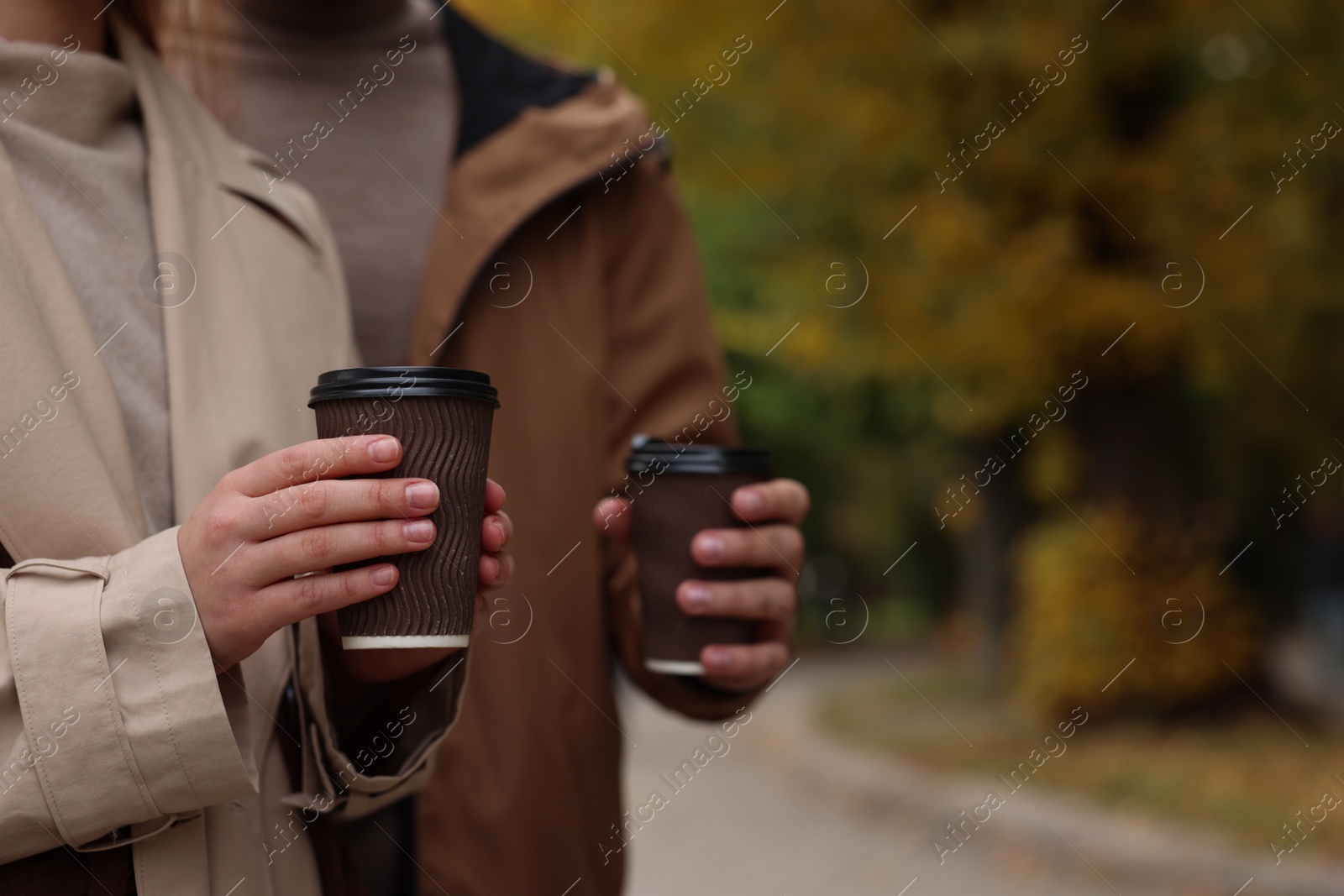 Photo of Happy young couple with cups of coffee spending time together in autumn park, closeup. Space for text