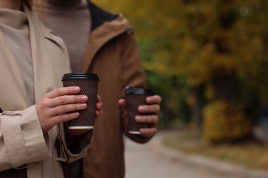 Happy young couple with cups of coffee spending time together in autumn park, closeup. Space for text