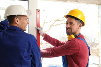 Photo of Workers using bubble level for installing window indoors