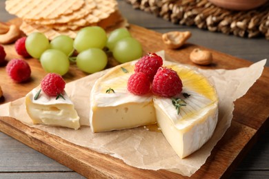 Photo of Brie cheese served with berries on wooden table, closeup