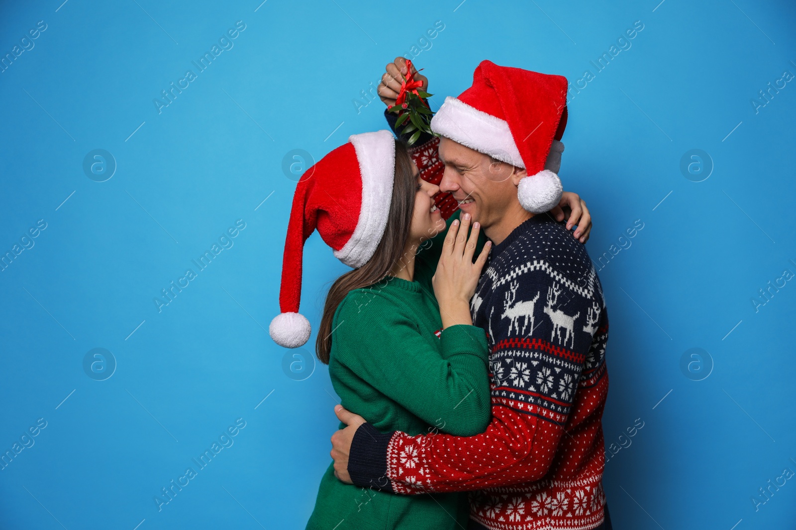 Photo of Happy couple standing under mistletoe bunch on light blue background