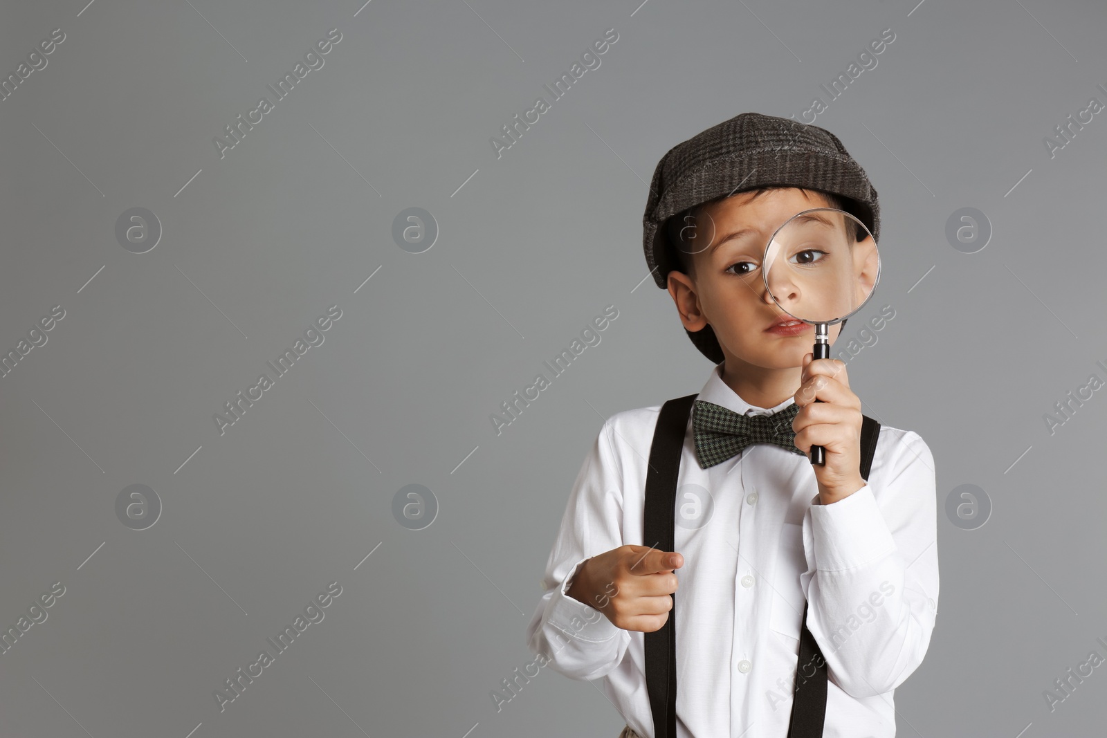 Photo of Little boy with magnifying glass playing detective on grey background. Space for text