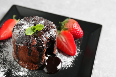 Delicious warm chocolate lava cake with mint and strawberries on plate, closeup