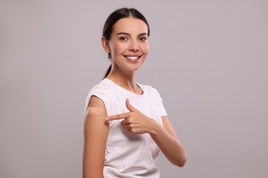 Photo of Woman pointing at sticking plaster after vaccination on her arm against light grey background