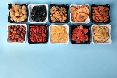 Bowls with dried fruits and nuts on light blue background, flat lay. Space for text