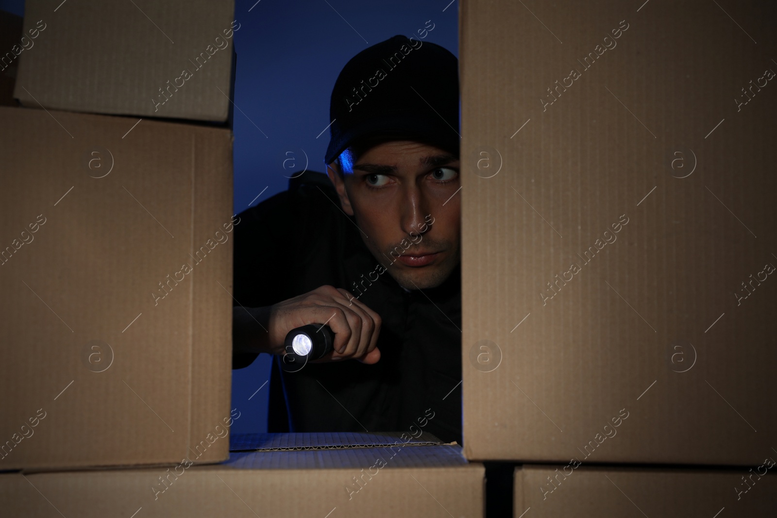 Photo of Security guard with flashlight looking through pile of cardboard boxes in dark room