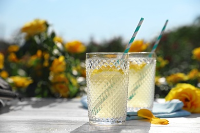 Photo of Glasses of refreshing lemonade on white wooden table in rose garden. Space for text