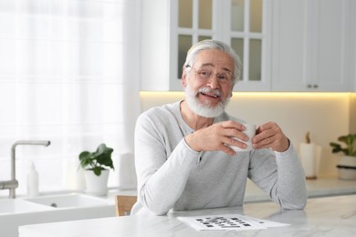 Photo of Senior man with cup of drink at table in kitchen