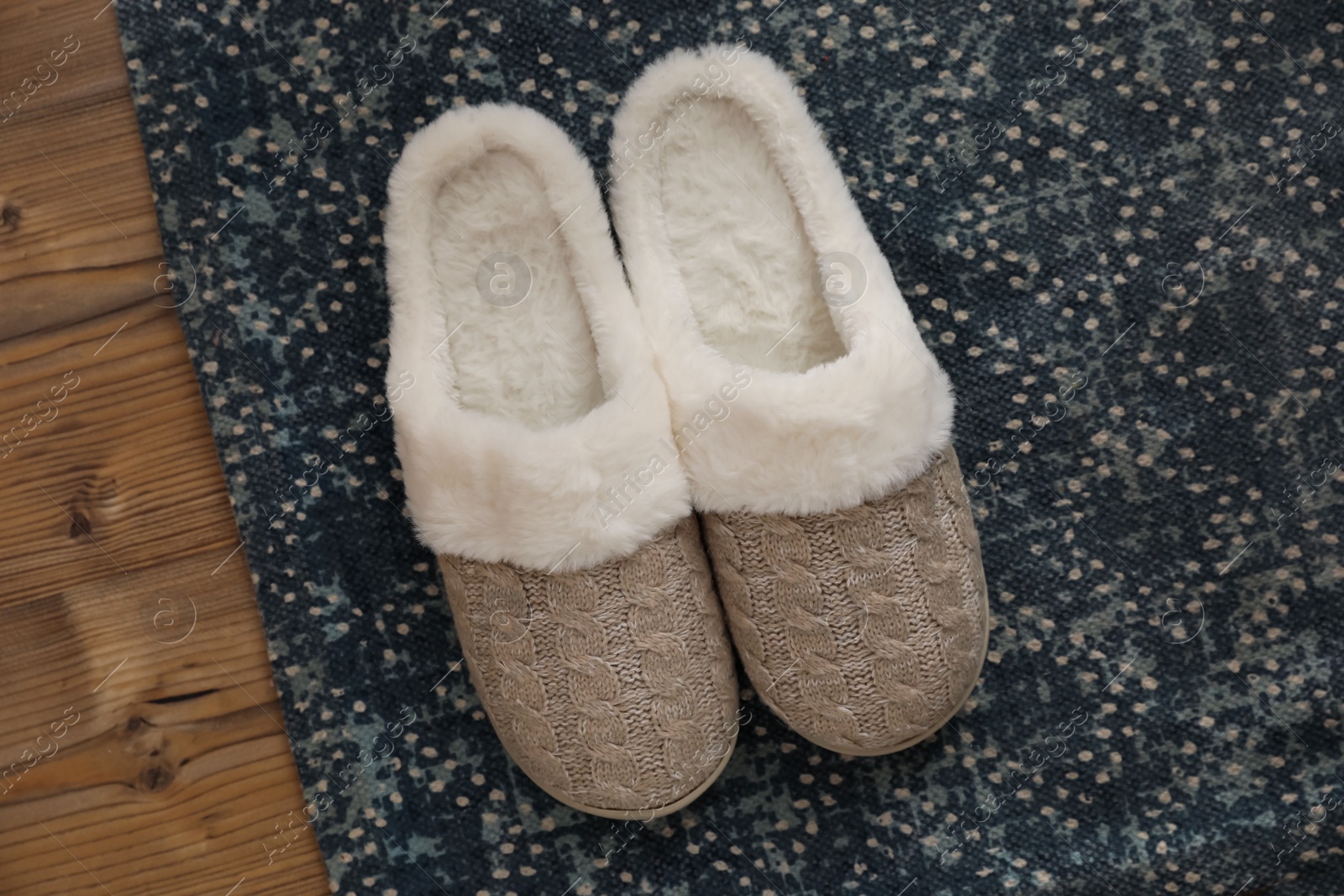 Pair of beautiful soft slippers and rug on wooden floor, top view Photo of Pair of beautiful soft slippers and rug on wooden floor, top view