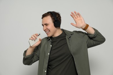 Photo of Handsome young man with headphones and smartphone singing on light grey background