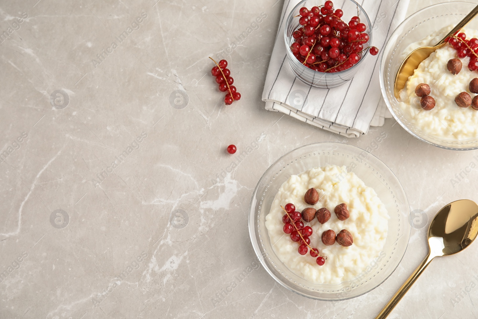 Photo of Creamy rice pudding with red currant and hazelnuts in bowls served on grey table, top view. Space for text