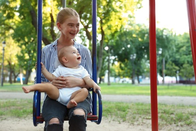 Photo of Teen nanny with cute little baby on swing outdoors. Space for text