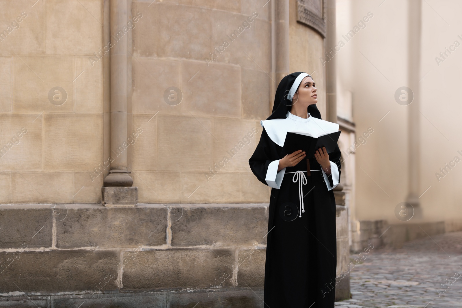 Photo of Young nun reading Bible near building outdoors