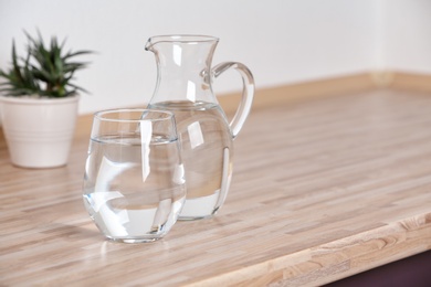 Photo of Glass and jug with fresh water on table in kitchen. Space for text