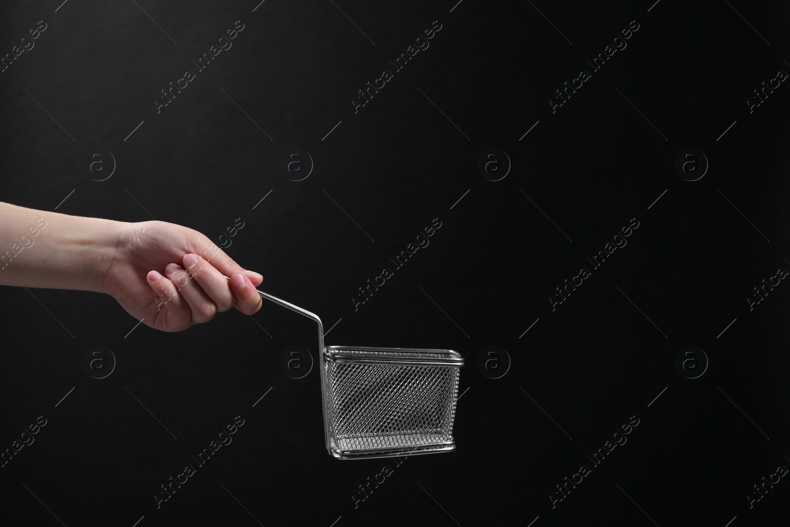 Photo of Woman holding metal basket for French fries on black background, closeup. Space for text
