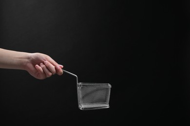 Woman holding metal basket for French fries on black background, closeup. Space for text