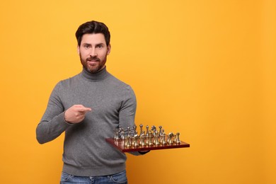 Handsome man holding chessboard with game pieces on yellow background. Space for text