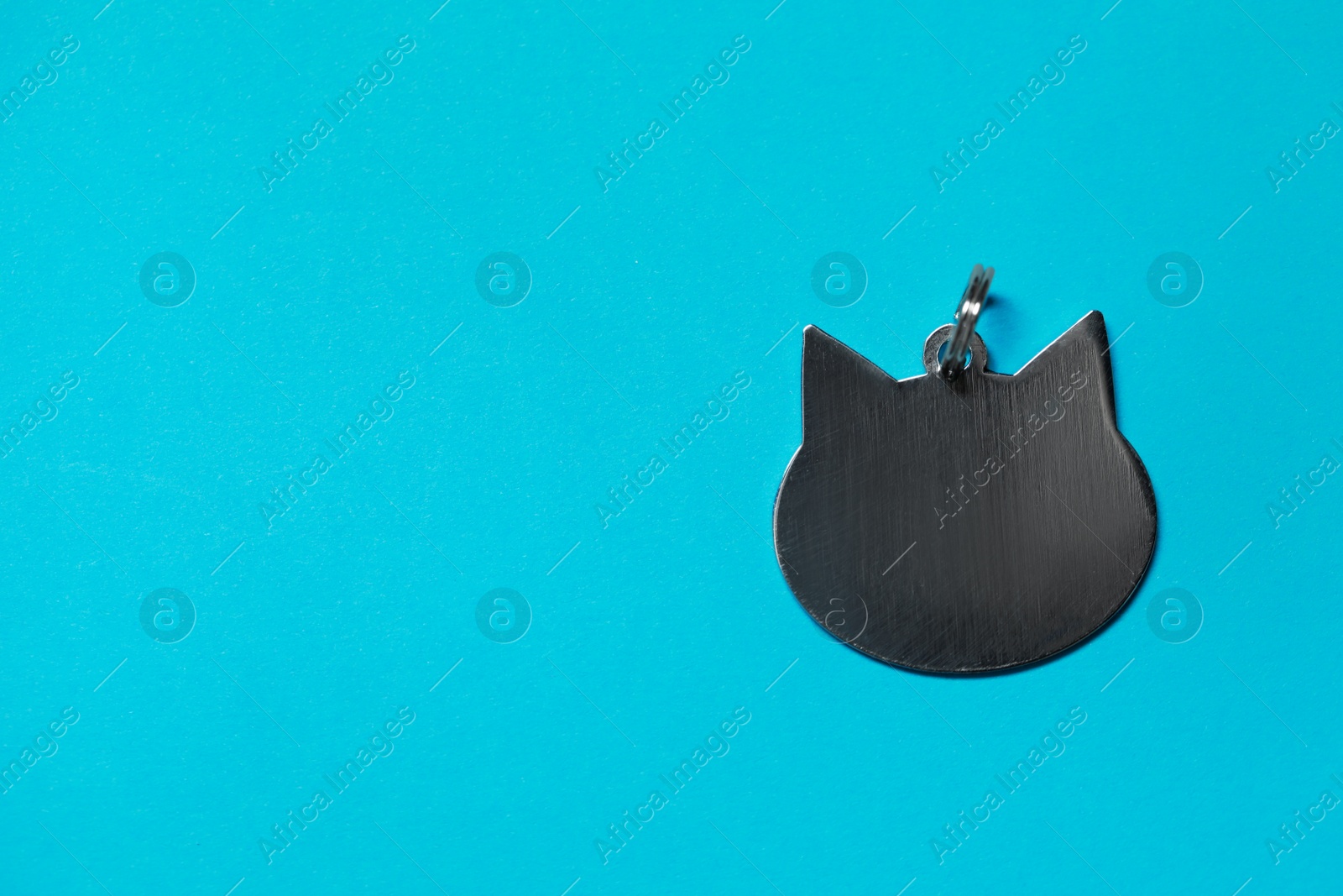 Photo of Silver pet tag in shape of cat with ring on light blue background, top view. Space for text