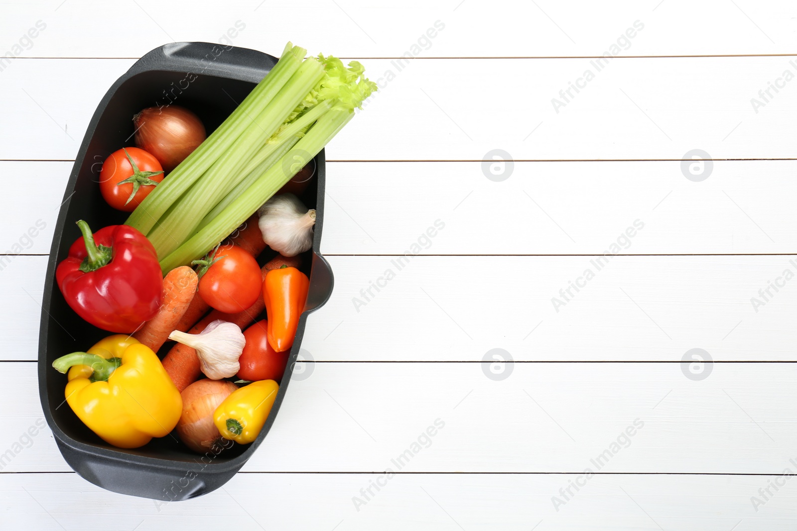 Photo of Black pot with fresh vegetables on white wooden table, top view. Space for text