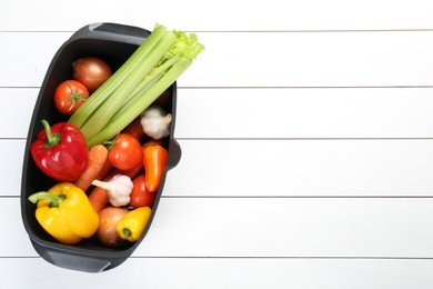 Photo of Black pot with fresh vegetables on white wooden table, top view. Space for text