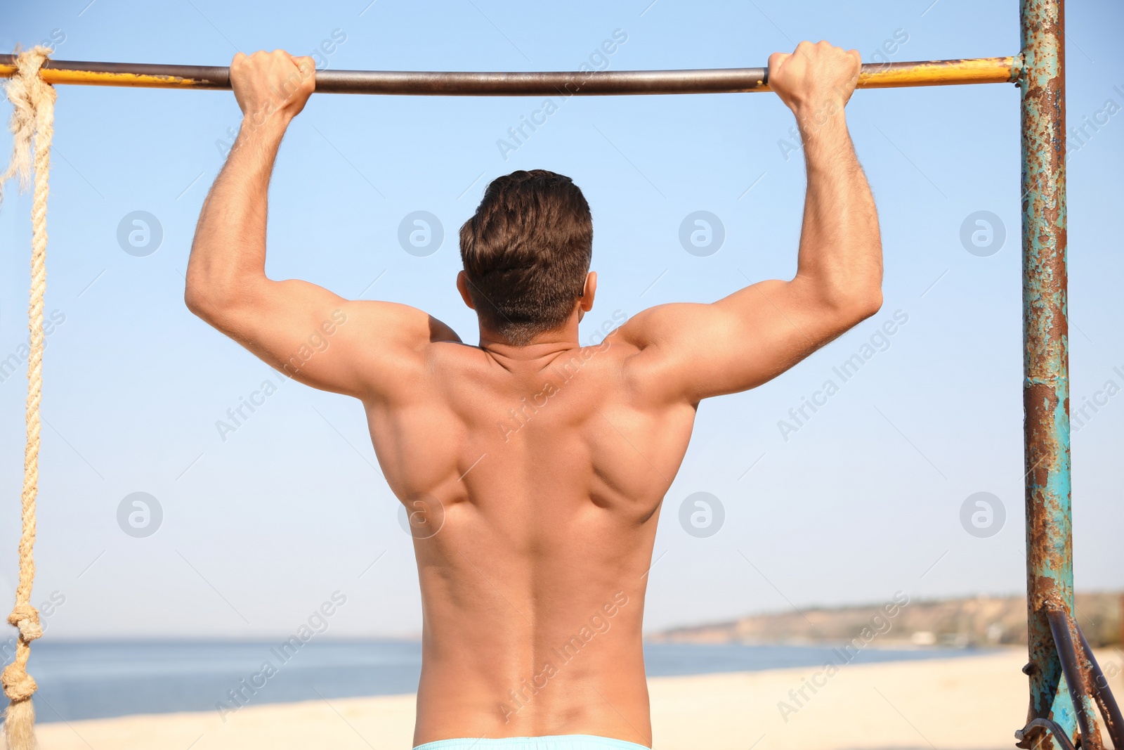 Photo of Man with slim body doing pull-ups
on beach